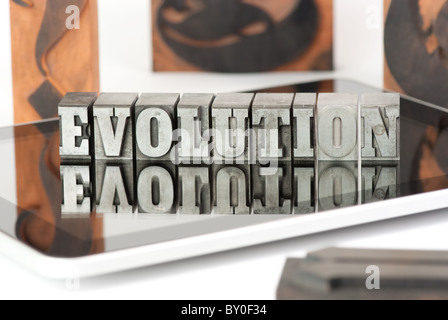 The word EVOLUTION in plumb letters, standing on a tablet pc, surrounded by wooden letters Stock Photo