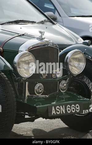 The front of a vintage Bentley car is shown, parked on a street next to more modern vehicles. Stock Photo