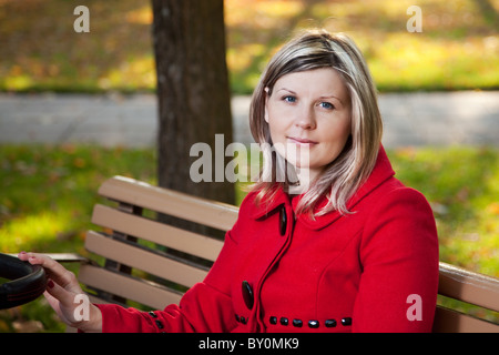 Blond woman in red coat holding handle or pram. Stock Photo