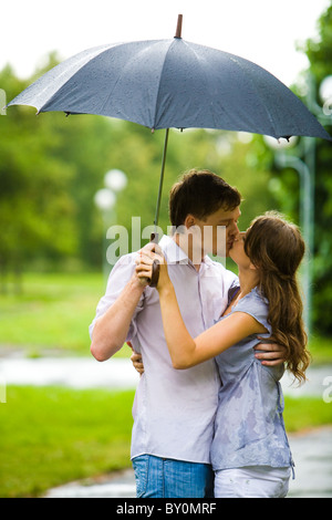 Portrait of romantic couple embracing and kissing each other under umbrella during rain Stock Photo