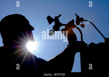 A meteorology specialist silhouetted against blue skies installing a weather station. Stock Photo