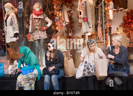 Four women sit outside a clothes shop on Oxford Street, London, UK Stock Photo