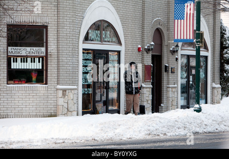 A man in front of a music store smoking a cigarette during a break from shoveling snow. Stock Photo