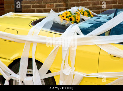 Paper ribbons festoon a yellow Alpha Romeo convertible car with sunflowers in the back seat at an Italian wedding Stock Photo