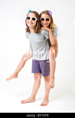 Two girls with sunglasses having fun one girl take the other a piggyback isolated on white Stock Photo