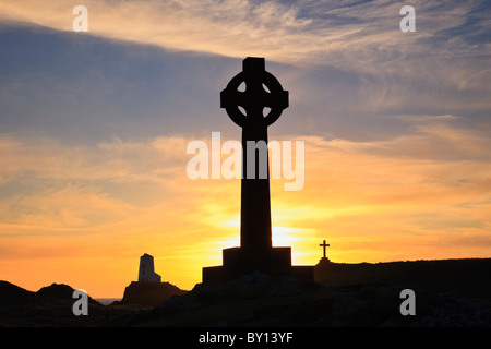 Sun setting behind St Dwynwen's Celtic cross and Twr Mawr lighthouse in silhouette on Llanddwyn Island. Newborough, Isle of Anglesey, North Wales, UK Stock Photo