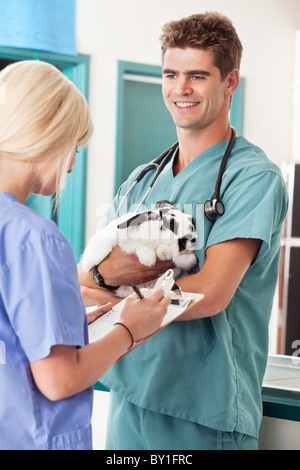 Portrait of a veterinarian holding rabbit with assistant taking report in animal hospital Stock Photo