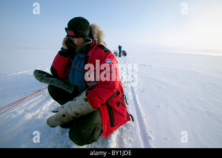 Norway, Finnmark Region. Dog sledding in the Arctic Circle - an explorer stops his husky team to make a phone call on a frozen Stock Photo