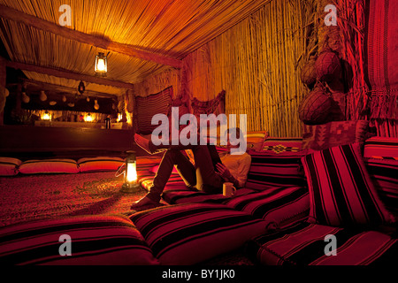 Oman, Wahiba Sands. A young lady relaxes with a book in the Nomadic Desert Camp. MR Stock Photo