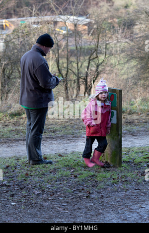 Young girl in winter clothes leaning against walking path sign with father Stock Photo