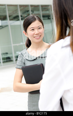 Asian businesswoman having conversation, office building as background Stock Photo