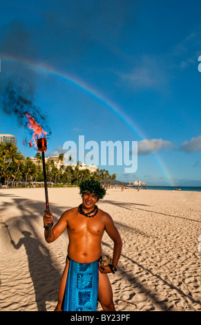 Native man with torch and rainbow and palm shadow on Waikiki Beach near the Hilton Hawaiian Village in Honolulu Hawaii in Oahu Stock Photo