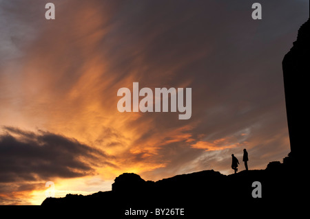 two people standing in silhouette at against a dramatic sky and clouds at sundown dusk, UK Stock Photo