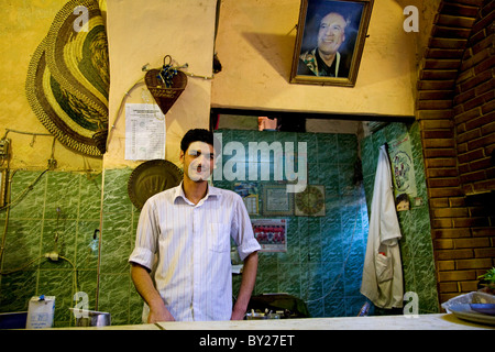Tripoli, Libya; A young Egyptian man working at a bar in the old Medina, with the portait Libya's President Colonel Gaddafi Stock Photo
