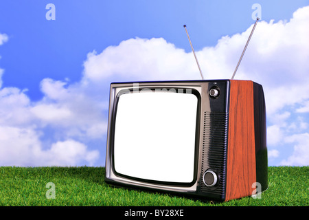 Photo of an old retro TV outdoors on grass with blue sky and white clouds in the background