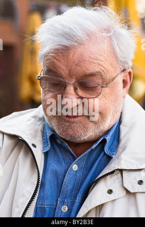 Elderly man sitting at sidewalk cafe, smiling, looking down Stock Photo