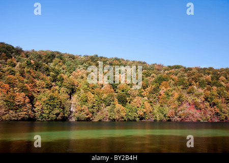 Landscape with early autumn forest on a hill, lake and blue sky Stock Photo