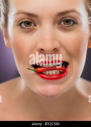 white blonde woman biting a chili pepper Stock Photo
