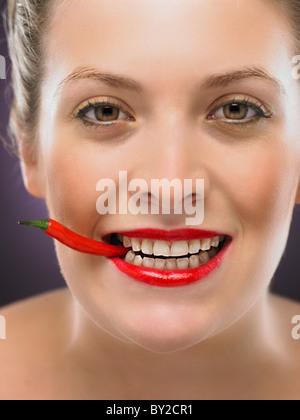 white blonde woman biting a chili pepper Stock Photo