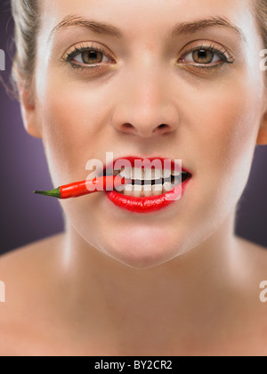 white blonde woman biting a chili pepper Stock Photo