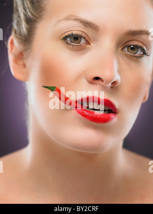 white blonde woman biting a chili pepper Stock Photo