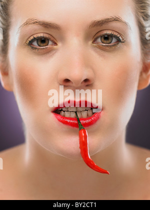 white blonde woman biting a chili pepper Stock Photo