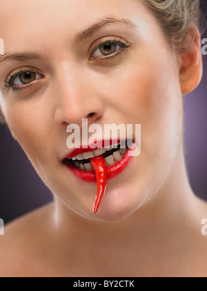 white blonde woman biting a chili pepper Stock Photo