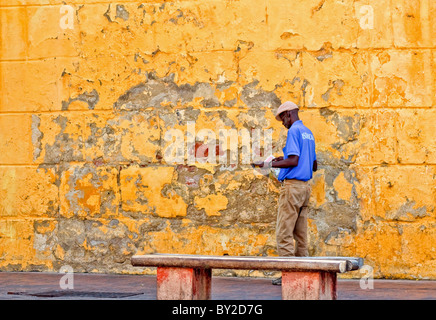Man in blue shirt reading paper in front of orange wall Stock Photo