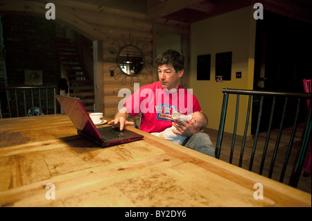 A man uses a laptop while holding his infant son in Tennessee. Stock Photo