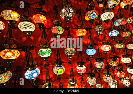 Mosaic Glass Lamps Grand Bazaar Istanbul Turkey // ISTANBUL, Turkey — Colorful mosaic glass lamps hang in tightly packed rows inside a shop in Istanbul's historic Grand Bazaar, their stained-glass panels catching the light in patterns of red, blue, amber and green. Each lamp is individually assembled from hand-cut glass fitted into a metal frame, continuing a craft rooted in Ottoman decorative traditions. The bazaar's lamp merchants are among its most visually distinctive traders, their shops a draw for the hundreds of thousands of visitors who pass through the market's roughly 60 covered stre Stock Photo