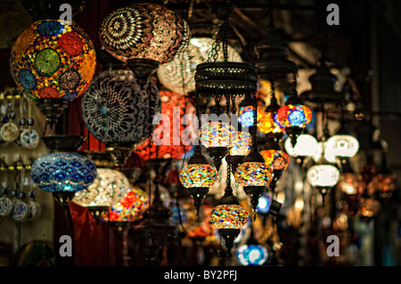 Mosaic Glass Lamps Grand Bazaar Istanbul // ISTANBUL, Turkey — Vibrant mosaic glass lamps crowd the shelves and ceiling of a shop in Istanbul's historic Grand Bazaar. The hand-assembled fixtures combine colored stained glass with metalwork frames, a craft that draws on Ottoman decorative traditions going back centuries. These lamps are among the most sought-after goods in the bazaar, which encompasses some 3,000–4,000 shops along roughly 60 covered streets and draws hundreds of thousands of visitors a day. Stock Photo