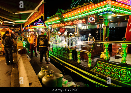 ISTANBUL, Turkey / Türkiye — Boats cooking fish for sandwiches on an open grill on the waterfront of Eminonu in Istanbul near the Galata Bridge spanning the Golden Horn. Customers buy the sandwiches on the dock and the cooks stay on the boat. Stock Photo