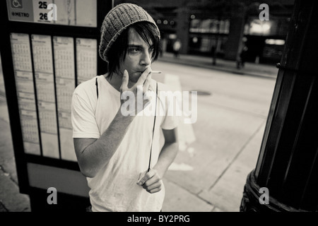 A homeless young adult smokes a cigarette in downtown Seattle while waiting for a bus Stock Photo