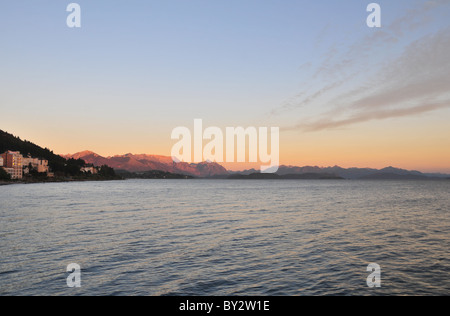 Cerro Lopez and Andean peaks glowing red in morning sunlight across waters of Lake Nahuel Huapi, Bariloche waterfront, Argentina Stock Photo