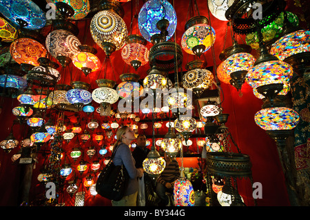 Mosaic Glass Lamps Grand Bazaar Istanbul Turkey // ISTANBUL, Turkey — A shop in Istanbul's historic Grand Bazaar glows with the light of mosaic glass lamps, their colored stained-glass panels and metalwork frames clustered from floor to ceiling. The hand-assembled fixtures are crafted individually, each pane of glass cut and fitted by hand into a metal armature — a process rooted in Ottoman decorative traditions. Lamp shops are among the most visually striking in the market, which draws an estimated 150,000–500,000 visitors a day across some 3,000–4,000 shops. Stock Photo