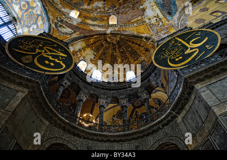 ISTANBUL, Turkey - Massive calligraphy medallions in Aya Sofya with the names of Allah, the Prophet Muhammad, the first four caliphs Abu Bakr, Umar, Uthman and Ali, and the two grandchildren of Mohammed: Hassan and Hussain, by the calligrapher Kazasker İzzed Effendi (1801–1877). Originally built as a Christian cathedral, then converted to a Muslim mosque in the 15th century, and now a museum (since 1935), the Hagia Sophia is one of the oldest and grandest buildings in Istanbul. For a thousand years, it was the largest cathedral in the world and is regarded as the crowning achievement of Byzant Stock Photo