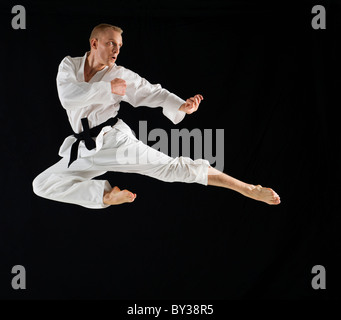 Young man performing karate kick on black background Stock Photo