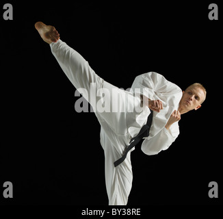 Young man performing karate kick on black background Stock Photo