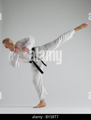 Young man performing karate kick on white background Stock Photo