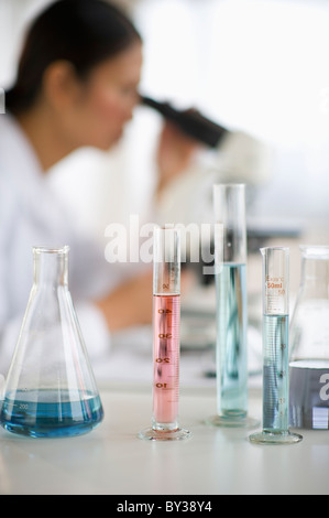 USA, New Jersey, Jersey City, Female scientist using microscope behind test tubes and flasks Stock Photo