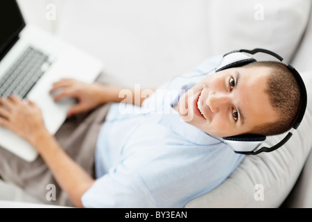 South Africa, Young man wearing headphones sitting on sofa and using laptop, high angle view Stock Photo