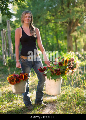 USA, Colorado, Young woman carrying buckets with sunflowers Stock Photo