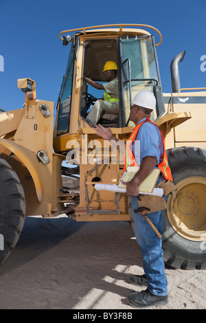Two construction workers talking by mechanical digger Stock Photo