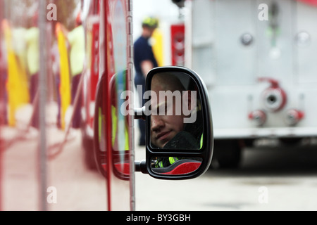 A firefighter reflection in the fire truck vehicle rear view side mirror and a firefighter in the background