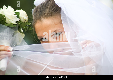 Close-up of young green-eyed bride holding veil by her face and looking at camera Stock Photo