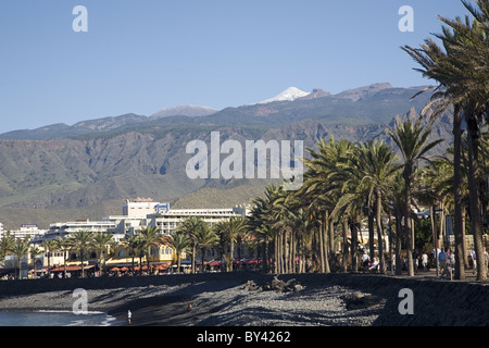 Promenade of Playa de las Americas with snow covered summit of the Pico del Teide in the background, Tenerife, Canaries, Spain Stock Photo