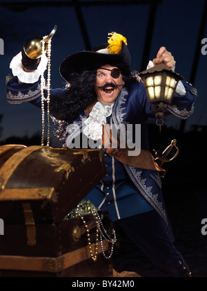 License and prints at MaximImages.com - Pirate with a lantern opening a treasure chest full of gold and jewels Stock Photo