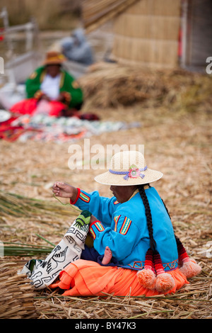 A woman sows while holding a baby on the floating islands of Uros on Lake Titicaca Stock Photo