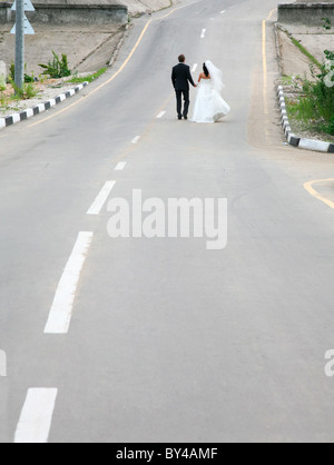 Conceptual image of newlyweds walking on road together Stock Photo
