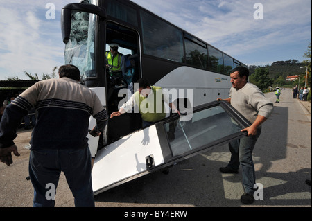 Three men pick up the door of a wrecked bus with shattered windscreen glass after a car crash Stock Photo